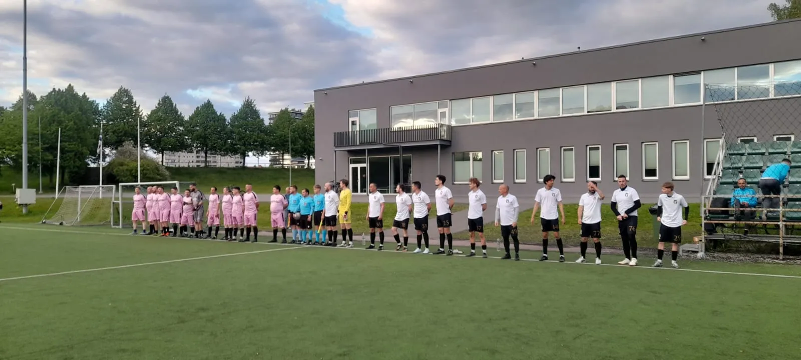 Rumori players in white lined up before a match, with the referees and the opposing team