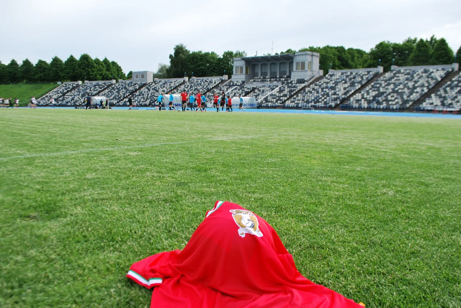 A red Rumori shirt with the club crest lying on the grass, with players warming up in the background