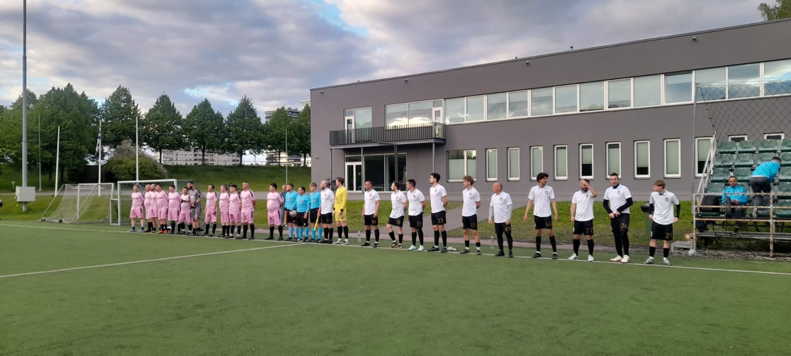 Rumori players in white lined up before a match, with the referees and the opposing team